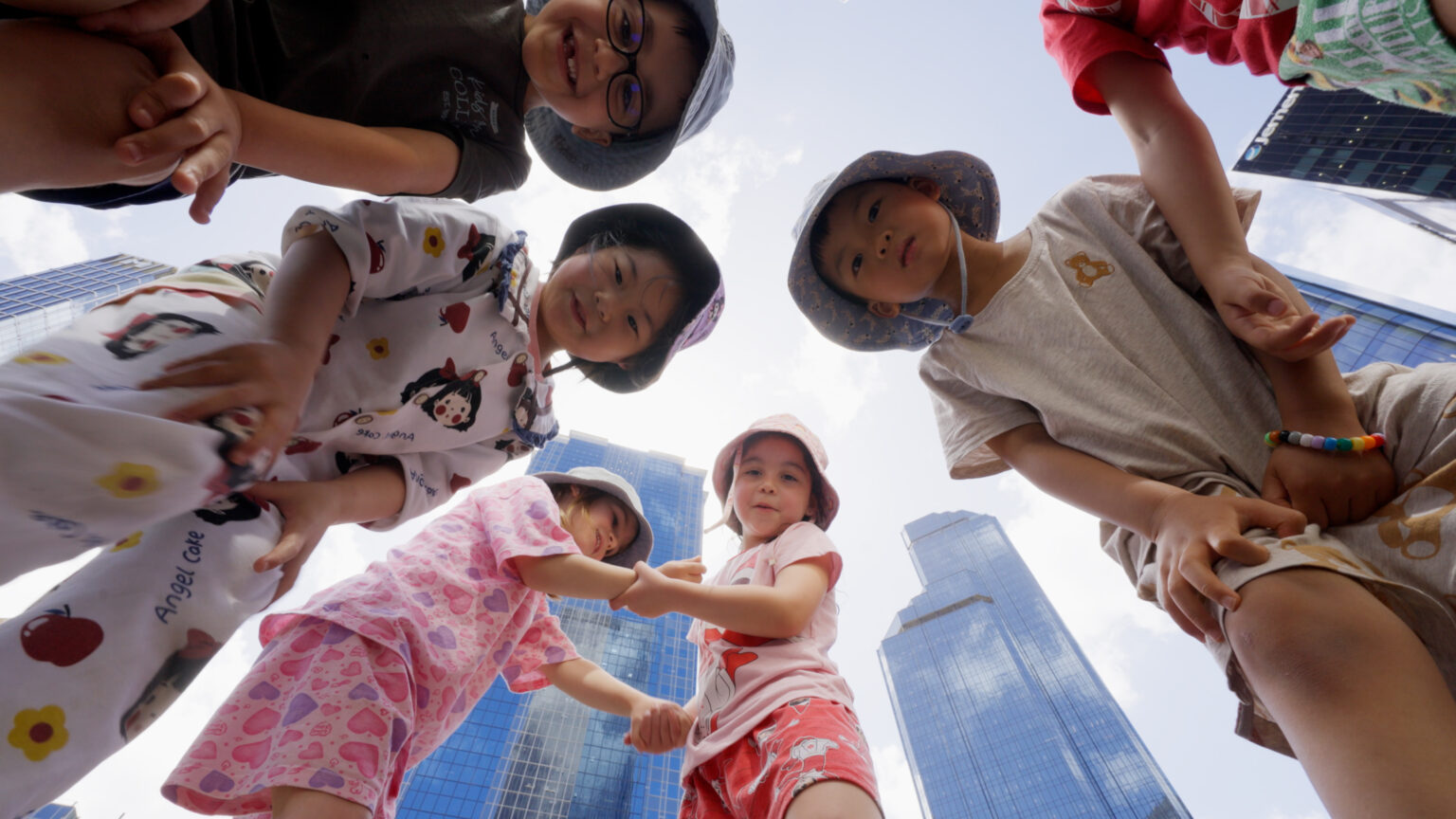 Kids are looking at the camera near tall buildings